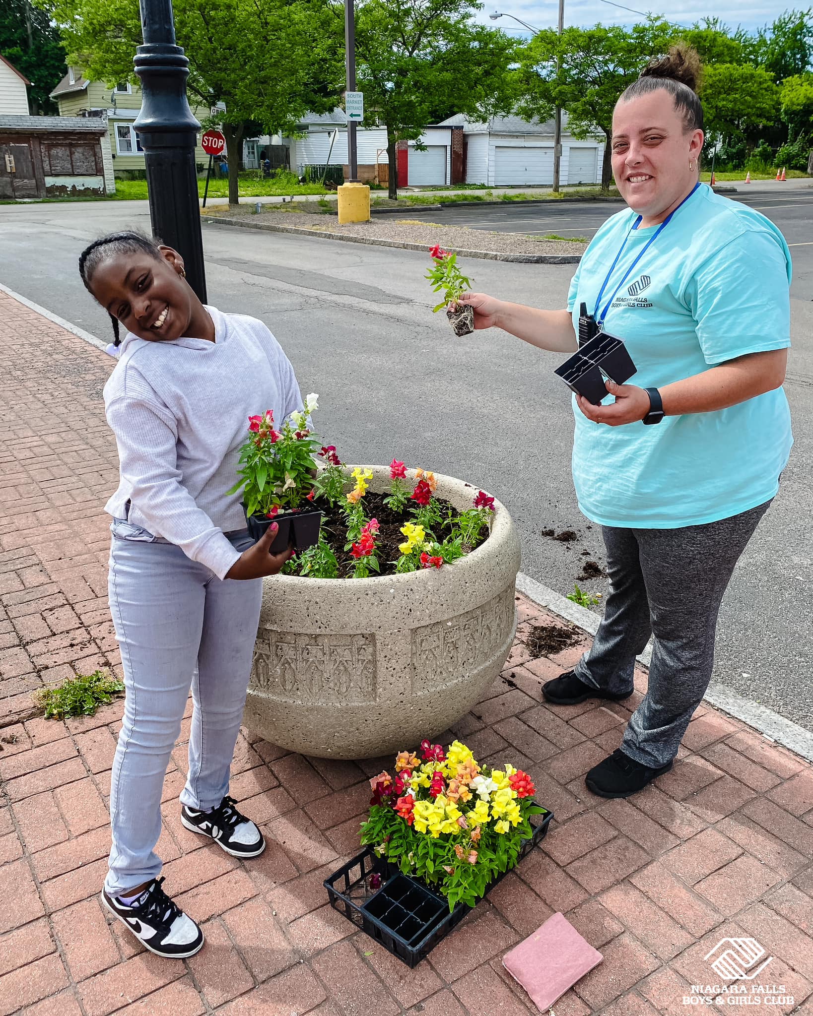 Volunteer opportunities in Niagara Falls mentoring youth planting flowers in a sidewalk planter outside the club.
